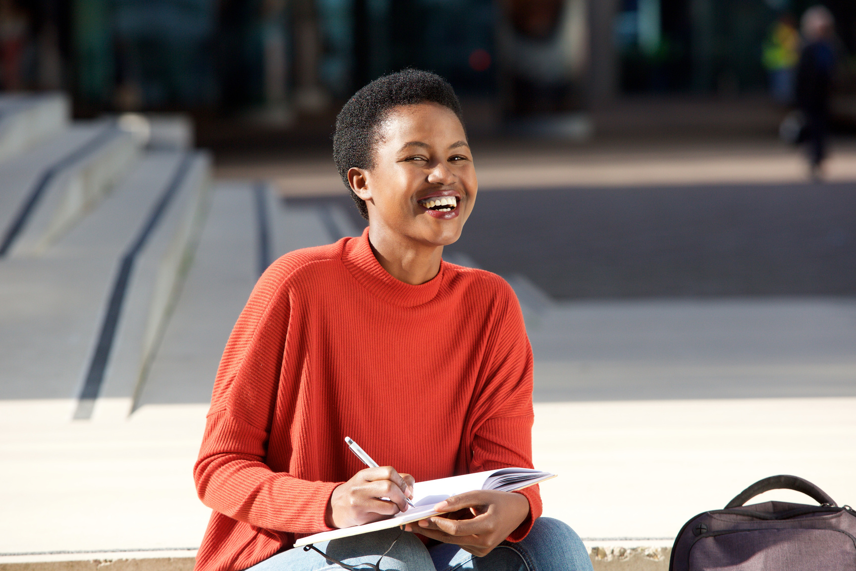 Happy Young Black Woman Writing in Book outside